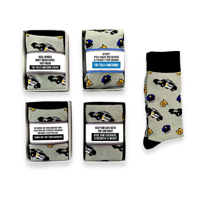 Puede incluir: Calcetines grises con un dise&ntilde;o de coche de polic&iacute;a y pu&ntilde;os y punteras negros. Los calcetines se presentan en cajas con etiquetas que dicen "REAL HEROES DON'T WEAR CAPES, THEY WEAR TOE-TALLY AWESOME SOCKS!" y otros mensajes.