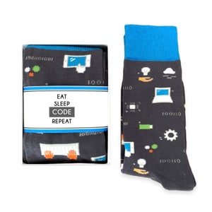 May include: A pair of black socks with a blue cuff. The socks feature a variety of computer-related icons, including a laptop, a cloud, a lightbulb, and a keyboard. The socks also have the text "Eat Sleep Code Repeat" on the box.