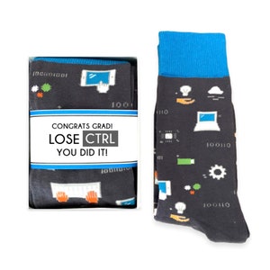 May include: A pair of black socks with a blue cuff and a colorful computer-themed design. The socks are packaged in a white box with the text "Congrats Grad! Lose Ctrl You Did It!" printed on the front.