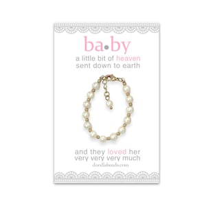 May include: A white pearl bracelet with a gold clasp and a small gold charm. The bracelet is on a white card with the text "ba.by a little bit of heaven sent down to earth and they loved her very very very much doodlebeads.com"