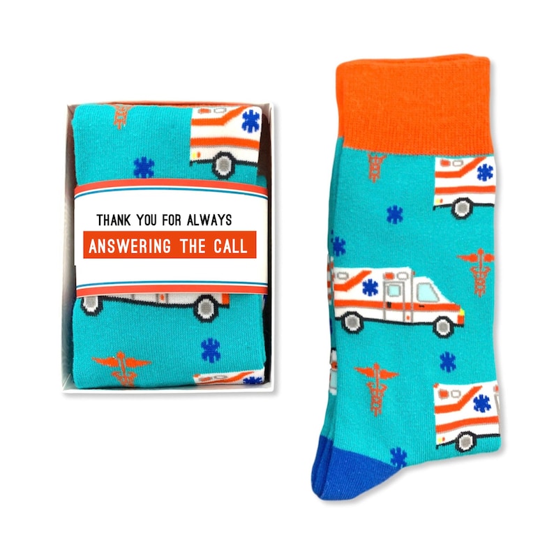 May include: A pair of blue socks with a white ambulance and red medical symbol pattern. The socks come in a white box with a red and white label that says "Thank you for always answering the call".