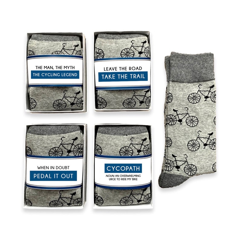 May include: Four pairs of gray socks with a black bicycle design. Each pair is packaged in a white box with a blue and white label. The labels have different sayings about cycling. The sayings are: "The man, the myth, the cycling legend", "Leave the road, take the trail", "When in doubt, pedal it out", and "Cycopath: Noun, an overwhelming urge to ride my bike".