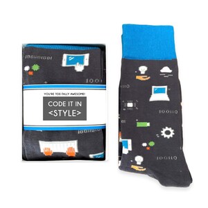 May include: A pair of black socks with a blue cuff. The socks feature a variety of computer-related icons, including a keyboard, a computer monitor, a cloud, a lightbulb, and a gear. The socks are packaged in a white box with the text "You're toe-tally awesome! Code it in <style>" printed on the front.