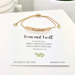 Puede incluir: Pulsera ajustable dorada con la inscripción "I can and I will". La pulsera está sobre una tarjeta blanca con la misma frase y el versículo bíblico Filipenses 4:13. La tarjeta también presenta la marca "DOODLE BEADS".