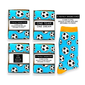 Könnte beinhalten: Fußballsocken, einige in Geschenkboxen und eine einzelne Socke. Die Socken sind hellblau mit einem Muster aus schwarz-weißen Fußbällen. Auf den Boxen steht "A 'TOE-TALLY' AMAZING PLAYER", "ONE TEAM ONE DREAM", "EAT SLEEP SOCCER REPEAT" und "A 'TOE-TALLY' AMAZING TEAM".
