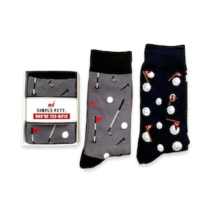 May include: Two pairs of golf-themed socks. One pair is gray with white golf balls, golf clubs, and flags. The other pair is navy blue with white golf balls and red flags. The socks are packaged in a white box with the text "SIMPLY PUTT, YOU'RE TEE-RIFIC".