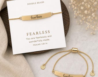 May include: Two gold-toned bracelets featuring a curved bar engraved with the word fearless in cursive script. One bracelet is attached to a white display card printed with DOODLE BEADS, FEARLESS, and the text You are fearlessly and wonderfully made. PSALMS 139:14.