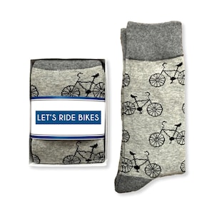 May include: A pair of gray socks with a black bicycle pattern. The socks are packaged in a white box with a blue and white label that reads "LET'S RIDE BIKES".