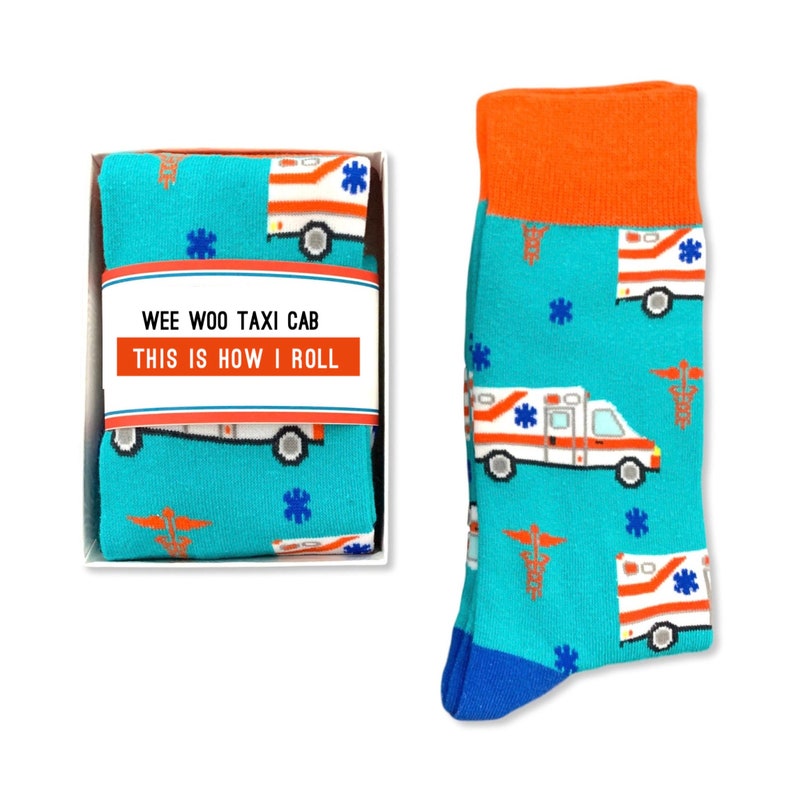 May include: A pair of blue and orange socks with a pattern of ambulances and medical symbols. The socks are in a white box with the text "Wee Woo Taxi Cab This Is How I Roll".