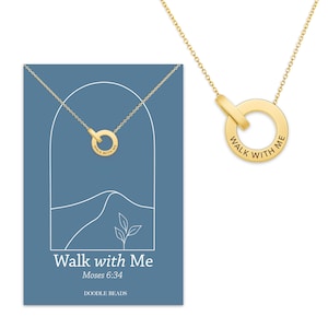 May include: A gold-colored necklace with a circular pendant that reads "Walk With Me." The necklace is displayed on a blue card with the same text, the Bible verse Moses 6:34, and a mountain and leaf design.
