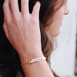 May include: Gold bracelet with a delicate chain and a bar charm engraved with the words "everyday i love you".