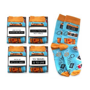 May include: Four boxes of socks with travel-themed designs and inspirational quotes. The quotes are "And so the adventure begins", "Collect moments not things", "Pack up let's fly away", and "To travel is to live".