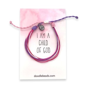May include: A colorful friendship bracelet with a silver charm that says "I am a child of God". The bracelet is on a white card with pink watercolor background and the website doodlebeads.com.