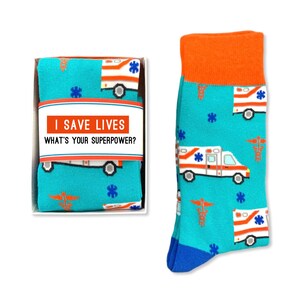 May include: A pair of blue socks with a white ambulance and red cross pattern. The socks come in a white box with the text "I save lives. What's your superpower?"