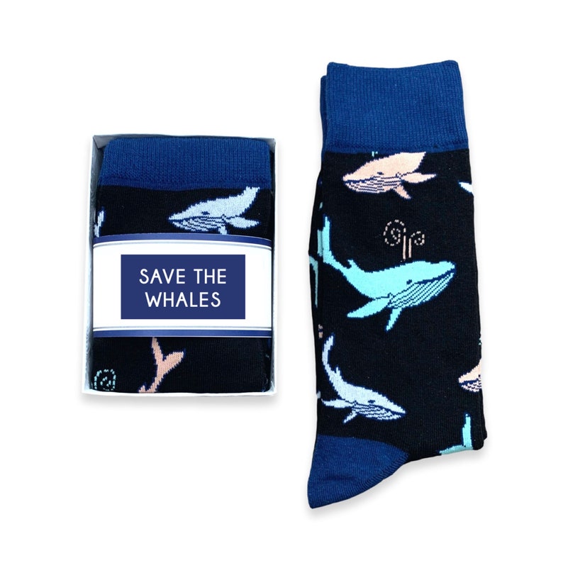 May include: A pair of black socks with a blue cuff and toe, featuring a pattern of light blue and pink whales. The socks are displayed next to a box containing a folded pair with the text "SAVE THE WHALES".