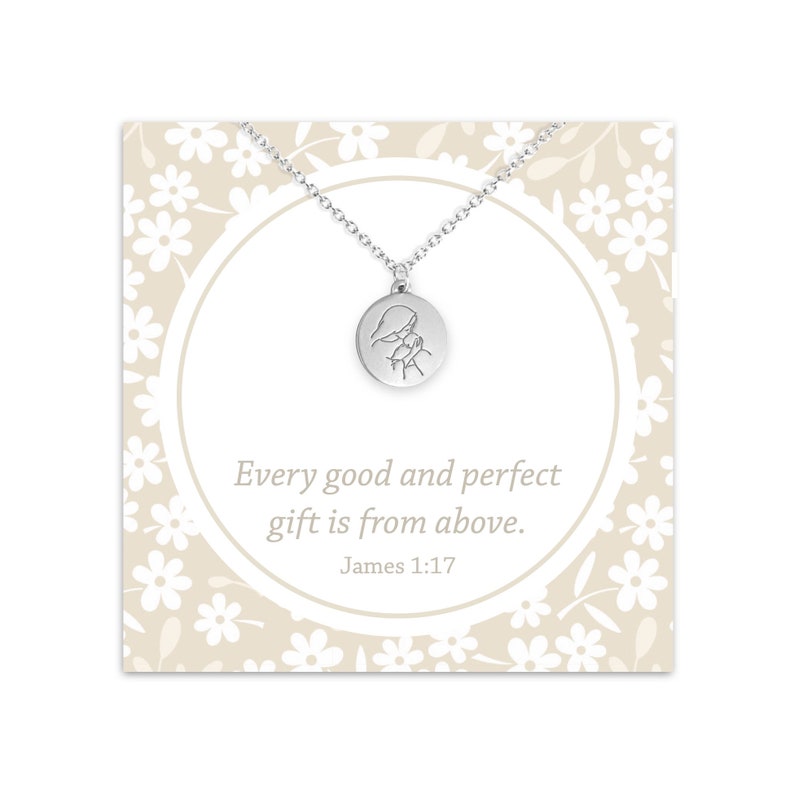 May include: Silver necklace with a round pendant featuring a simple line drawing of a person praying. The card reads "Every good and perfect gift is from above. James 1:17"