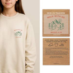 Puede incluir: Una sudadera color crema con el texto "WALK WITH ME" y "MOSES 6:34" impreso en un diseño de montaña verde y marrón. También se incluyen instrucciones de transferencia con plancha para camisas, sombreros o bolsos.