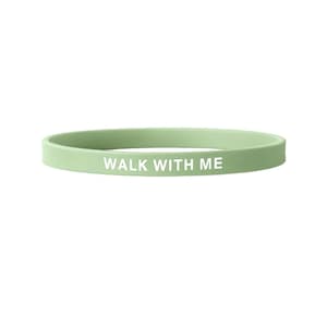 May include: A light green silicone wristband with the white text "WALK WITH ME". The band is a solid color and appears to be made of a flexible material. The text is centered on the band.
