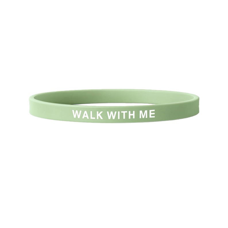 May include: A light green silicone wristband with the white text "WALK WITH ME". The band is a solid color and appears to be made of a flexible material. The text is centered on the band.