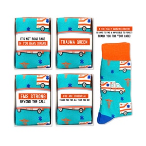 May include: Four boxes of socks with different designs and sayings. The socks are blue with a white ambulance and red cross pattern. The boxes have the following sayings: "It's not road rage if you have sirens", "Trauma Queen", "EMS Strong Beyond the Call", and "You are essential thank you for all that you do!"  A single sock is shown on the right side of the image. The sock is blue with a white ambulance and red cross pattern. The top of the sock is orange.
