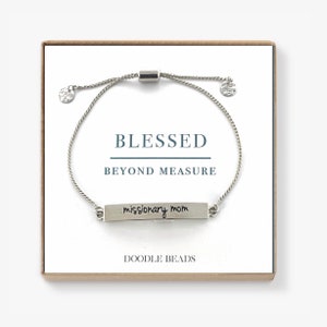 May include: Silver bracelet with a silver bar charm that says "missionary mom" and a silver slider bead. The bracelet is in a box with the words "Blessed Beyond Measure" and "Doodle Beads" printed on it.