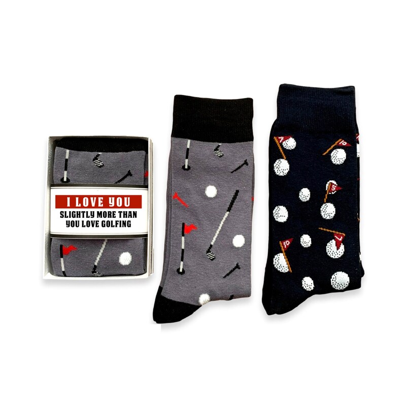 May include: A gift box containing a pair of gray socks with a golf club and ball pattern and a pair of navy blue socks with a golf ball and flag pattern. The box has a white label with the text "I love you slightly more than you love golfing."