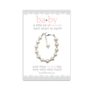 May include: A white pearl bracelet with a silver clasp and a small charm. The card reads "ba.by a little bit of heaven sent down to earth and they loved her very very very much doodlebeads.com"