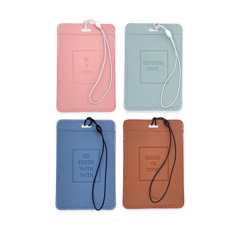 May include: Four different colored leather ID badge holders with lanyards. The holders are light pink, light blue, brown, and light green. Each holder has a different inspirational quote printed on the front. The quotes are "Be a Light", "Gathering Israel", "Go Forth With Faith", and "Called to Serve".