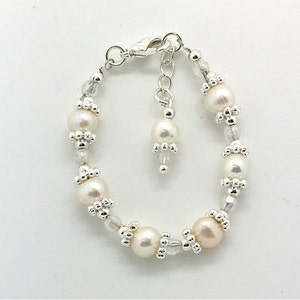 May include: A delicate silver bracelet with a small charm and white pearls. The bracelet is made with small silver beads and clear crystals.