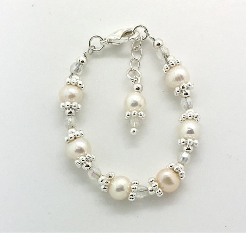 May include: A delicate silver bracelet with a small charm and white pearls. The bracelet is made with small silver beads and clear crystals.