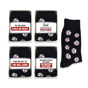 Könnte beinhalten: Vier Schachteln Socken mit Baseball-Motiven und verschiedenen Botschaften auf der Vorderseite. Die Botschaften lauten: "To the man who stole my heart", "Dad thanks for being my biggest fan even when I strike out", "Take me out to the ball game" und "No grass stains, no glory, no bruises, no story".