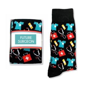 May include: A pair of black socks with a colorful pattern of medical symbols, including a stethoscope, a first aid kit, and a doctor's coat. The socks come in a white box with the words "FUTURE SURGEON" printed on the front.