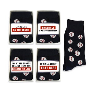 Könnte beinhalten: Vier Schachteln mit marineblauen Socken, auf denen weiße Baseballs aufgedruckt sind. Jede Schachtel hat einen anderen Baseball-Spruch auf einem weißen Etikett. Die Sprüche lauten "Living Life By The Seams", "Baseball Is My Favorite Season", "The Other Sports Are Just Sports Baseball Is A Love", und "It's All About That Base".