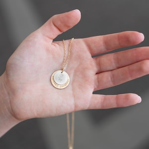 Puede incluir: Un collar de oro con un colgante de doble cara. La parte delantera del colgante tiene un pequeño diseño de flor. La parte posterior del colgante está grabada con las palabras "hija querida".