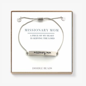 May include: Silver bracelet with a silver bar charm that says "missionary mom" in cursive. The bracelet is on a white background with a card that says "Missionary Mom, A piece of my heart is serving the Lord, Doodle Beads".
