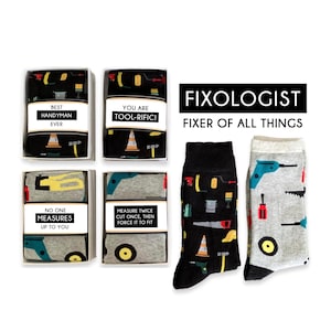 May include: Four gift boxes with different tool-themed designs and sayings. The boxes contain socks with a black and white design featuring tools and a gray and white design featuring tools. The socks are labeled "Fixologist, Fixer of All Things".