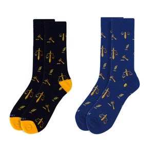 May include: Two pairs of socks with a law theme. One pair is navy blue with gold scales of justice, gavel, and quill designs. The other pair is black with the same gold designs.