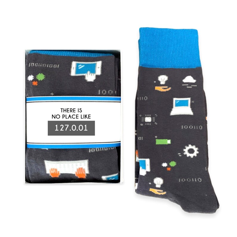 May include: A pair of black socks with a blue cuff. The socks feature a variety of computer-related icons, including a laptop, a cloud, a lightbulb, and a keyboard. The socks also have the text "THERE IS NO PLACE LIKE 127.0.0.1" printed on them.