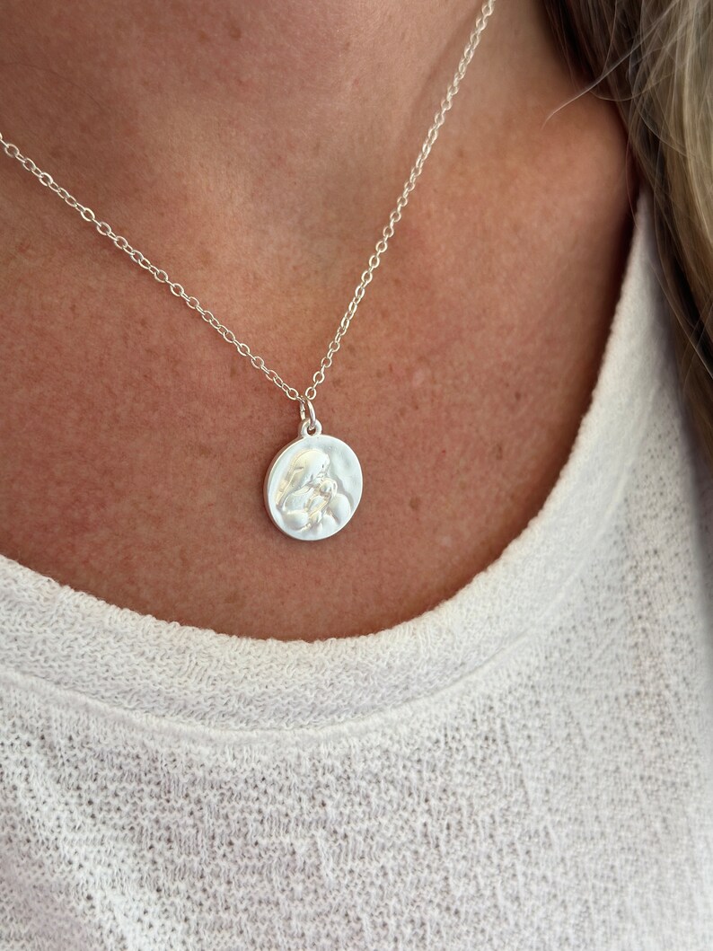 May include: A silver chain necklace with a round pendant featuring a detailed embossed design. The pendant is slightly textured.