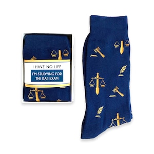 May include: A pair of blue socks with a gold pattern of scales of justice, gavel, and quill pens. The socks are in a white box with a label that reads "I have no life I'm studying for the bar exam".