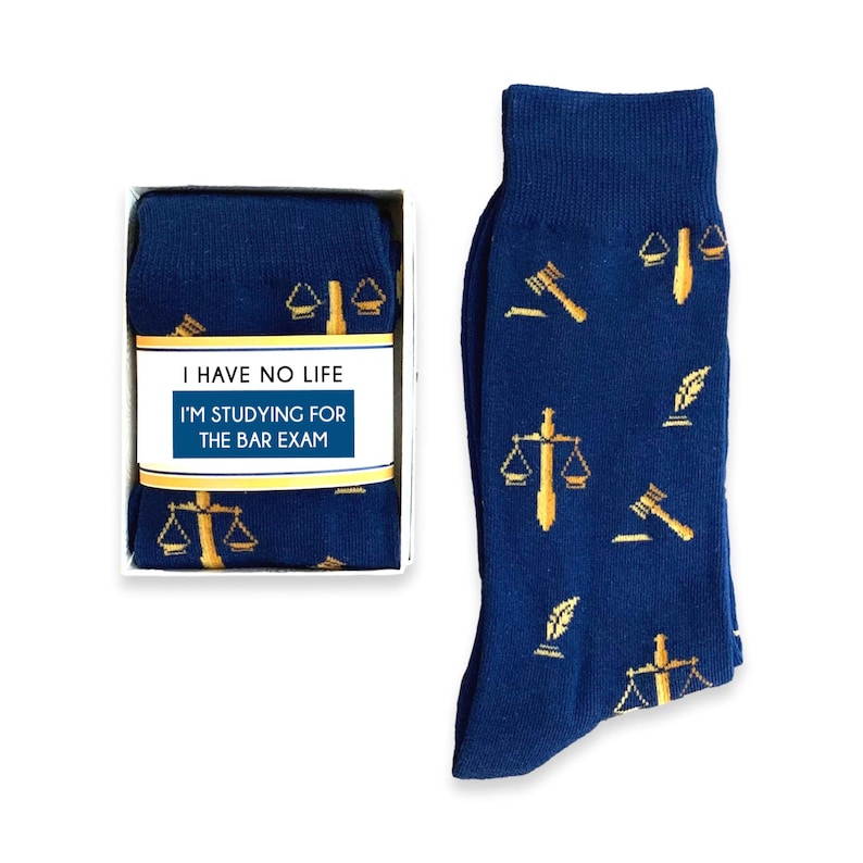 May include: A pair of blue socks with a gold pattern of scales of justice, gavel, and quill pens. The socks are in a white box with a label that reads "I have no life I'm studying for the bar exam".