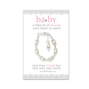 May include: A white pearl bracelet with a silver clasp and a small pearl charm. The bracelet is on a white card with the text "ba.by a little bit of heaven sent down to earth and they loved her very very very much doodlebeads.com"