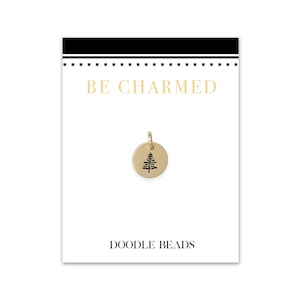 May include: Gold charm with a small tree design, on a white card with the text "BE CHARMED" and "DOODLE BEADS".