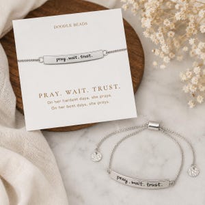 Può includere: Un braccialetto regolabile color argento con una barra metallica curva incisa con il testo pray. wait. trust. Il braccialetto è presentato su un cartoncino bianco con il nome del marchio DOODLE BEADS e il testo stampato PRAY. WAIT. TRUST. On her hardest days, she prays. On her best days, she prays.