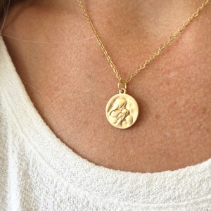 May include: A gold chain necklace with a round pendant featuring a raised image of two figures embracing.