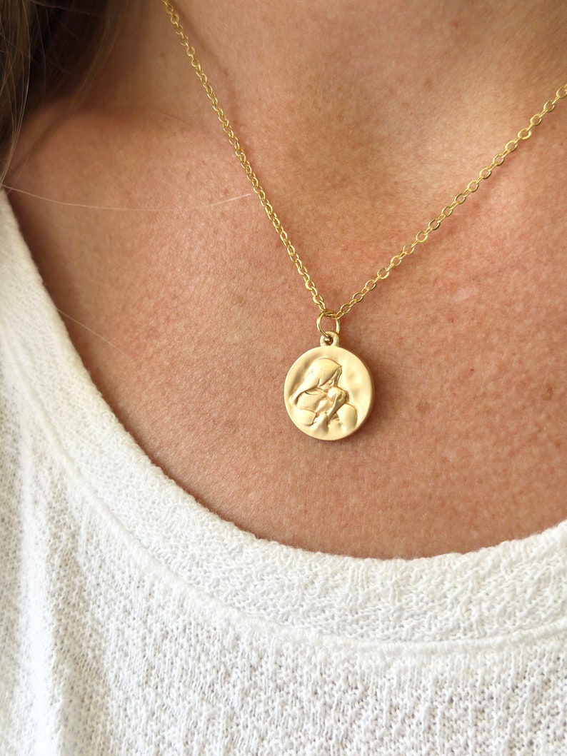 May include: A gold chain necklace with a round pendant featuring a raised image of two figures embracing.