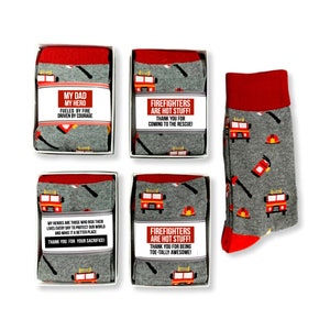 May include: Four white boxes with red trim contain pairs of gray socks with red fire truck and firefighter themed designs. The socks have a red top. The boxes have labels with text that reads "My Dad My Hero Fueled by Fire Driven by Courage", "Firefighters Are Hot Stuff! Thank You for Coming to the Rescue!" and "Firefighters Are Hot Stuff! Thank You for Being Toe-Tally Awesome!"