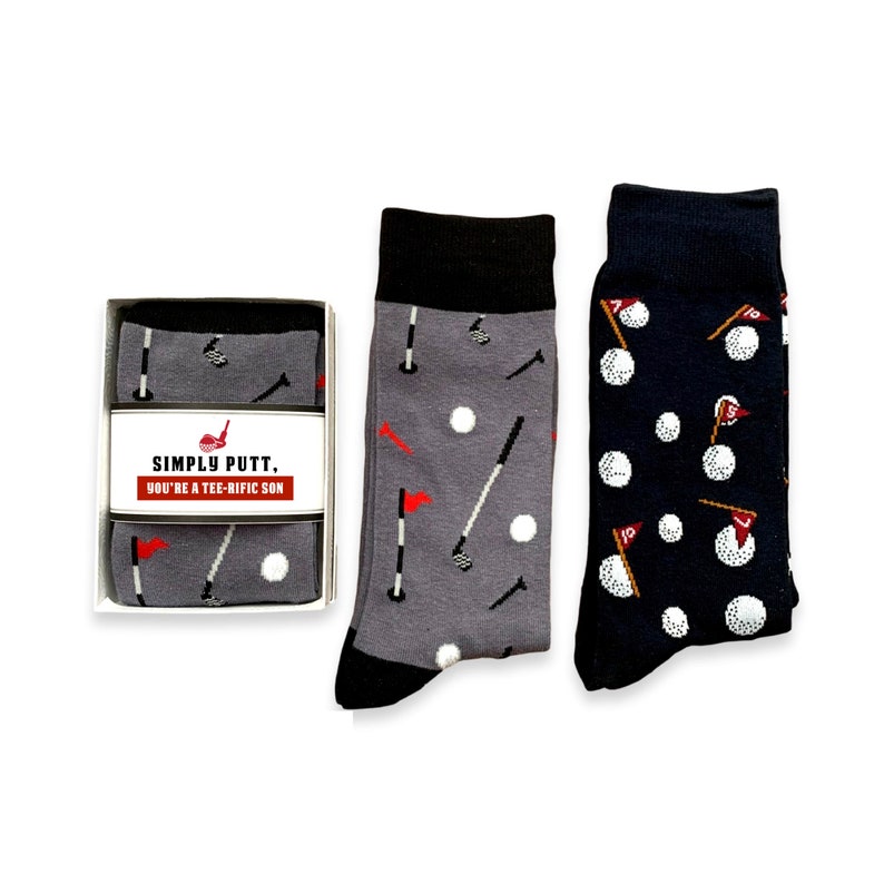 May include: Two pairs of socks with a golf theme. One pair is gray with white golf balls, golf clubs, and flags. The other pair is navy blue with white golf balls and flags. The socks come in a box with the text "Simply Putt. You're a Tee-Rific Son."