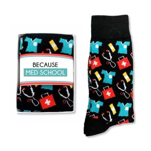 May include: A pair of black socks with a colorful pattern of medical symbols, including stethoscopes, first aid kits, and scrubs. The socks come in a white box with the text "Because Med School".