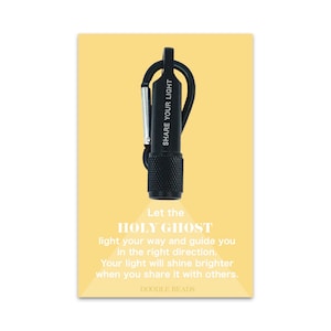 May include: A black keychain flashlight with a carabiner clip. The flashlight has the words "SHARE YOUR LIGHT" printed on the side. The text below the flashlight reads "Let the HOLY GHOST light your way and guide you in the right direction. Your light will shine brighter when you share it with others. DOODLE BEADS."